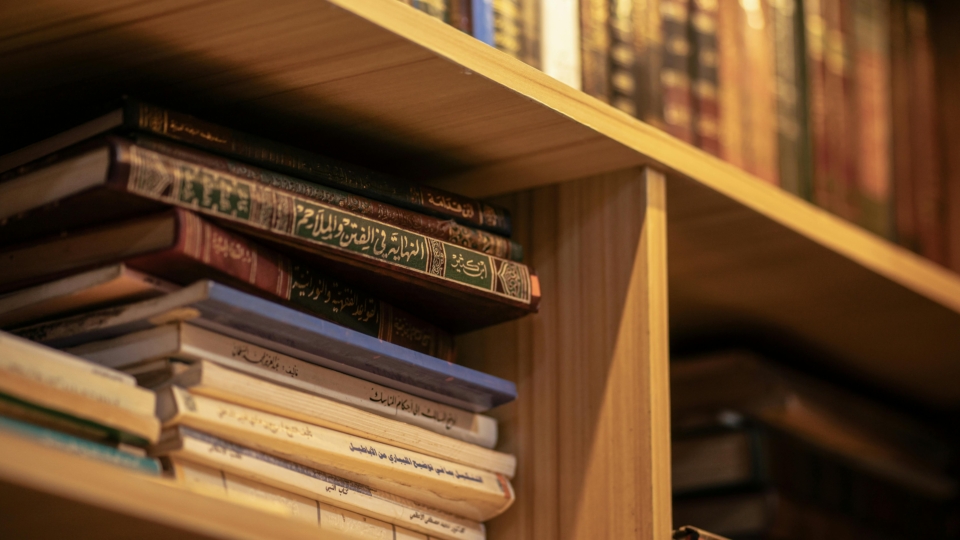 A stack of Islamic religious books on a wooden shelf, highlighting Arabic scripts and cultural significance.