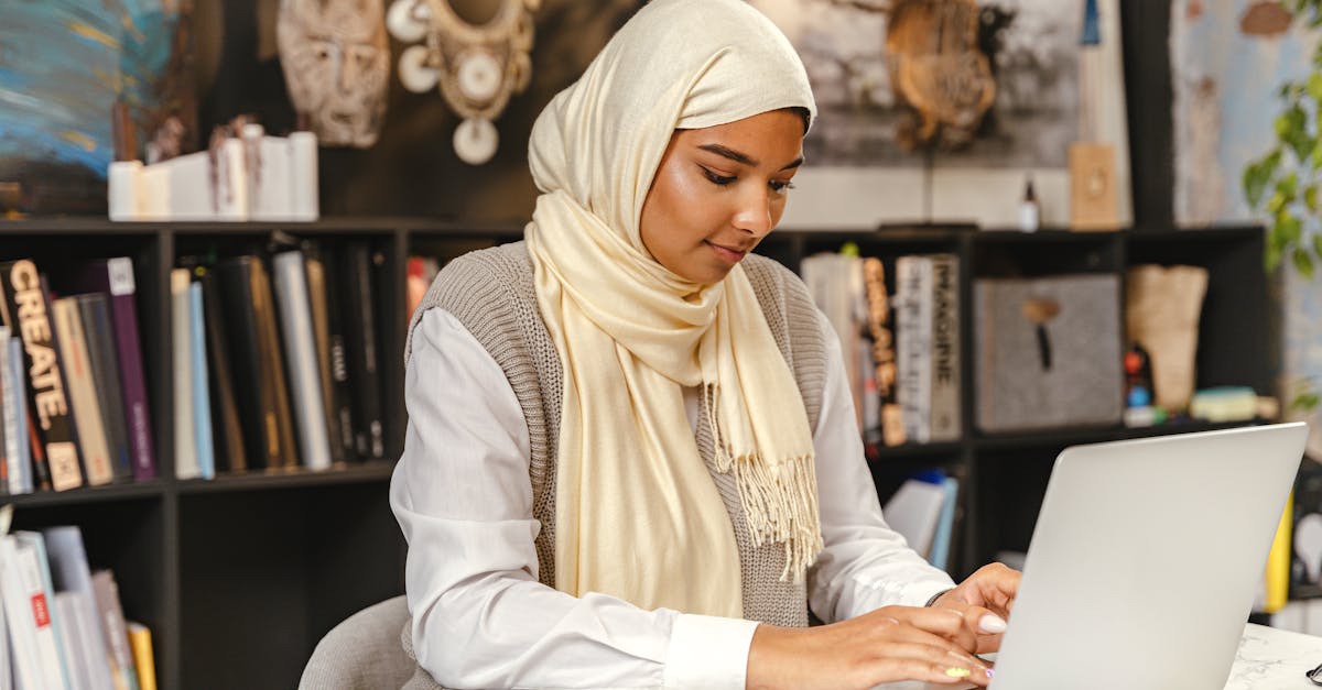 A Muslim woman in a hijab working on a laptop in a contemporary office setting, focused and professional.